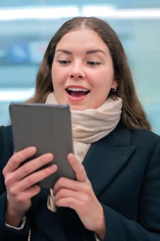 young woman in a black coat and beige scarf sitting inside a modern subway train, reading on an e-reader. She enjoys a quiet moment during her daily commute.