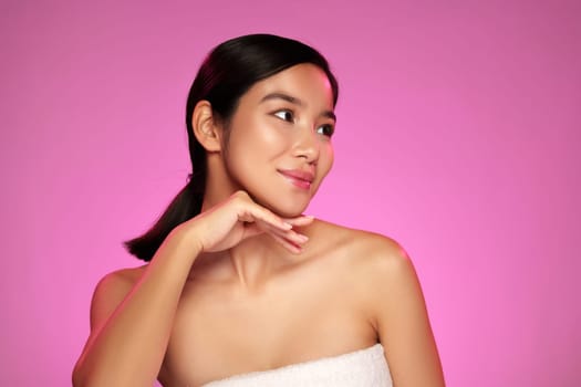 A woman in a strapless outfit is smiling softly, showing a relaxed demeanor while resting her chin on her hand against a bright pink backdrop, capturing a cheerful atmosphere.