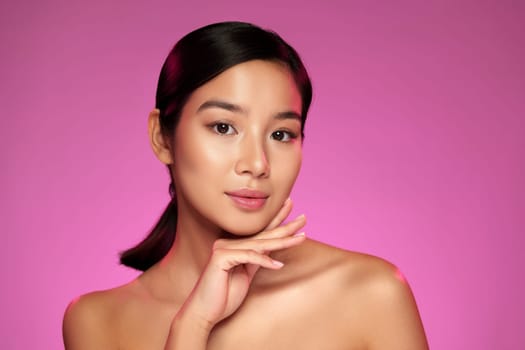 A model adorned with subtle makeup poses gracefully against a vibrant pink background. The expertise in her application highlights contemporary beauty trends.