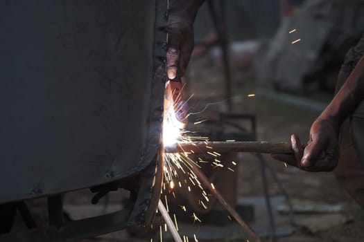 Sparks fly as a worker uses a welding tool on metal structures outside.
