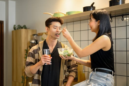 Happy young couple sharing a healthy salad in the kitchen.