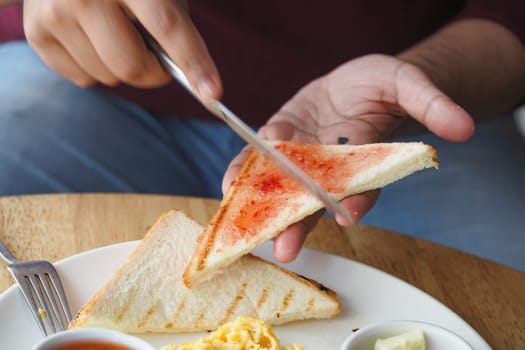A person cuts jam-topped toast while seated for breakfast.