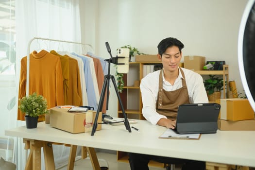 Male online seller in apron working on digital tablet, managing orders and preparing shipments.