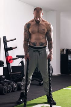concentrated shirtless sportsman standing with ropes during functional workout at gym, concept of fitness and active lifestyle