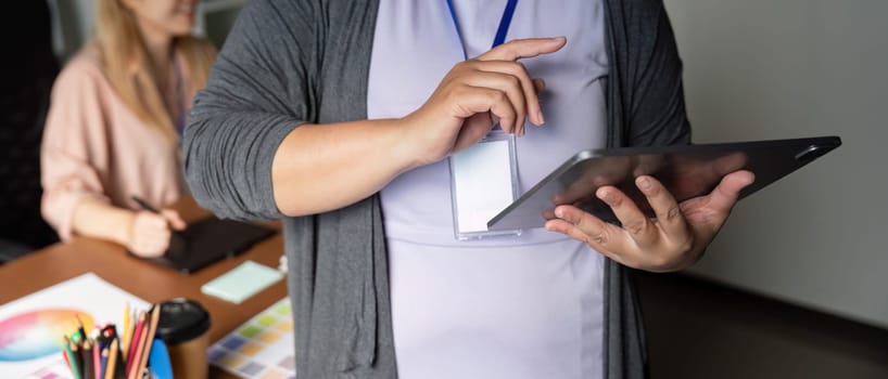 A graphic designer showcasing design ideas on a tablet, engaging in collaboration with a colleague in a vibrant creative office environment.