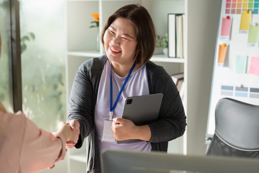A graphic designer smiling while shaking hands with a colleague, showcasing teamwork and collaboration in a modern creative workspace.