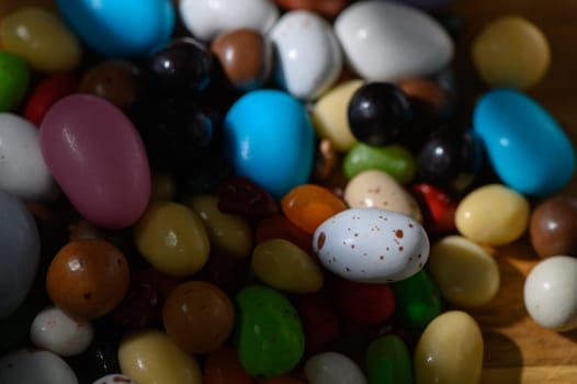 A vibrant collection of candies in diverse colors and shapes scatter across a natural wooden background.