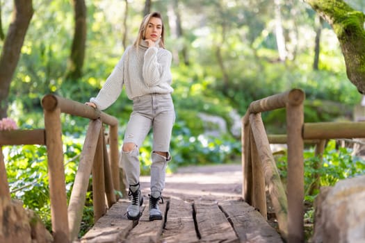 Young woman wearing casual clothing is standing on a wooden bridge in a forest