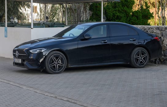 Gaziveren Cyprus -03.02.2025 A modern black sedan rests quietly in a driveway surrounded by vibrant greenery under a warm afternoon sun.