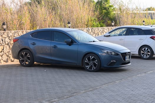 Gaziveren Cyprus -03.02.2025 A sleek blue sedan rests peacefully between lush greenery and stones at dusk, exuding calm and modern elegance.