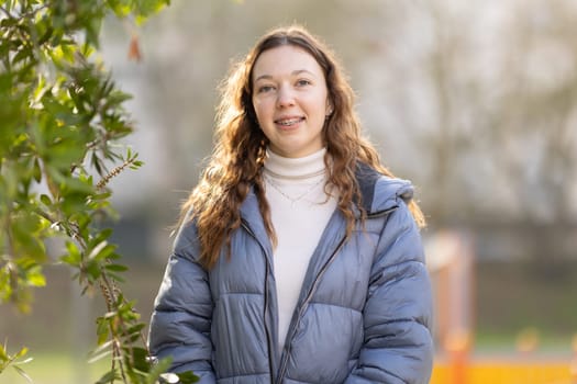 Portrait of a cheerful young woman smiling outdoors, wearing braces and a winter coat