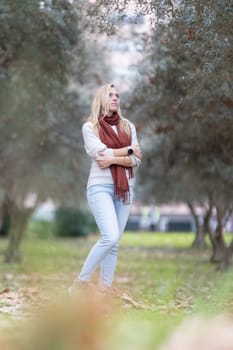Blonde woman standing in a park with olive trees looking up, enjoying the autumn day