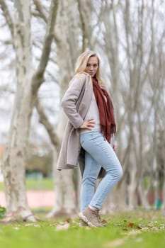 Fashionable woman wearing a coat and scarf enjoying a relaxing day in a park during the fall season