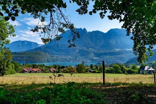 A beautiful mountain range with a lake in the foreground. The mountains are covered in trees and the lake is calm and clear. The scene is peaceful and serene, with a sense of tranquility and beauty Annecy lake, France