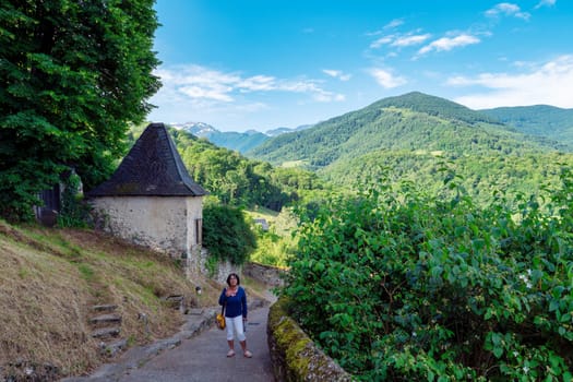 A woman is walking down a path in a forest. The path is surrounded by trees and the sky is clear