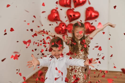 Children enjoy heart-shaped confetti. Balloons are in the background.Valentines Day concept
