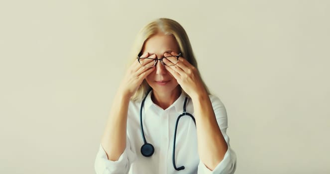 Tired middle-aged woman doctor working with documents while sitting at desk in medical clinic office