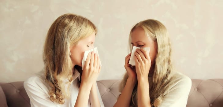 Sick exhausted middle-aged woman mother and adult daughter together sneezing blow nose using tissue at home