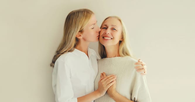 Portrait of adult daughter kissing her happy smiling caucasian middle aged mother on studio background