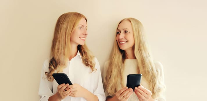 Two caucasian women with mobile phone looking at each other, middle aged mother and adult daughter together