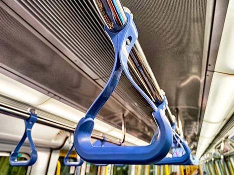 Close-up view of a blue handrail in a subway train with commuters in the background, highlighting public transport usage during rush hour.