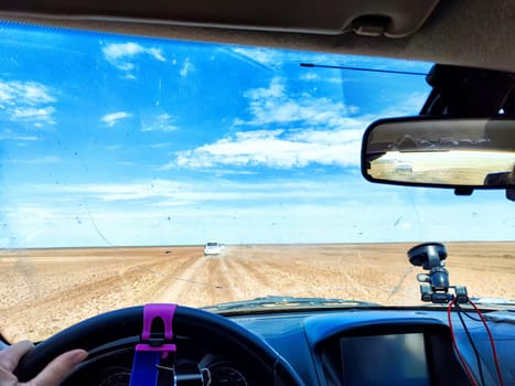 A driver navigates an open road with a cracked windshield while surrounded by green fields and a bright blue sky filled with clouds.