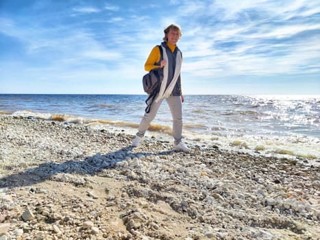 A woman strolls by the water's edge at the beach, contemplating life's journey amidst the autumn scenery and gentle waves.