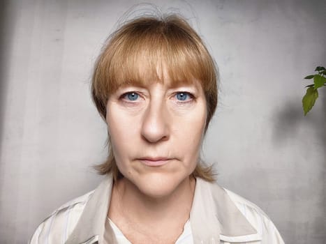 A middle-aged woman with blonde hair poses for a lifestyle blog photo in a simple indoor setting, appearing serious and somewhat unhappy.