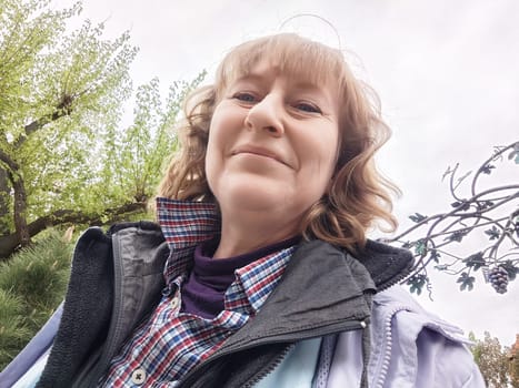 Blonde woman captures a cheerful selfie while exploring nature in a park on her travel journey.