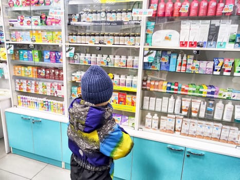Kirov, Russia - December 28, 2024: Young child stands at a pharmacy counter, observing various health products and medicines on display.