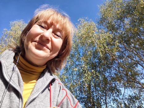 Blonde woman captures a joyful moment on her nature adventure, surrounded by vibrant autumn foliage and clear blue skies.