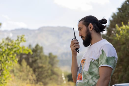A man in a rugged outdoor setting uses a walkie-talkie, for security or emergency coordination. His serious demeanor and remote location search-and-rescue worker, park ranger, or survivalist.