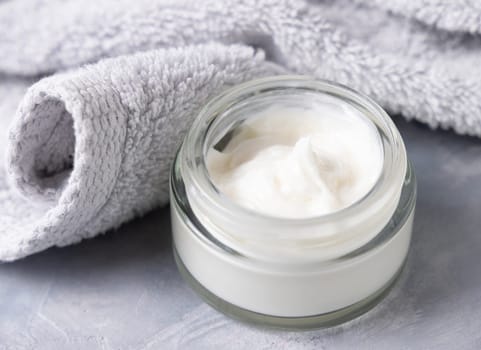 Opened cream jar near light gray bath towel closeup. Natural organic cosmetics for facial care. Lifestile scene of skincare, essence of Spa and Wellness, macro cream texture