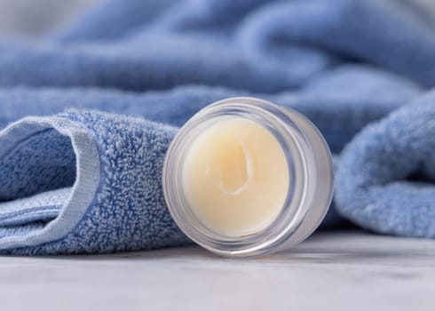 Opened lip balm jar near blue bath towel closeup, copy space. Herbal cosmetic product for mens and woman daily lipcare and personal care