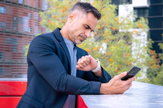 professional middle-aged businessman in a suit checking his smartphone and smartwatch. The modern city background highlights a fast-paced, connected lifestyle focused on productivity and efficiency.