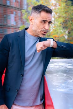 A middle-aged businessman in a suit checking his smartwatch with a focused expression. The modern city background highlights a professional and time-conscious lifestyle.