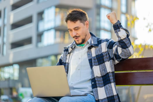 Overjoyed happy mature man working on laptop netbook screaming in delight triumph winner gesture celebrate success game money win outdoors. Happy adult guy tourist sitting on downtown city street.