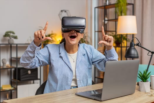 Surprised Indian woman freelancer testing VR headset while sitting at home office table. Young businessman girl making presentation using new gadget during remote working online at home. Lifestyle.