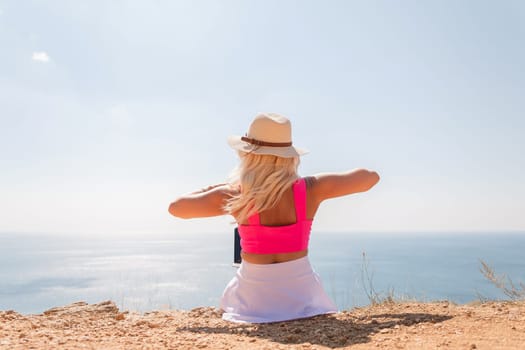 A woman in a pink top and straw hat is sitting on a beach, looking out at the ocean