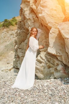 A woman in a white dress is standing on a rocky beach. Concept of serenity and tranquility, as the woman is enjoying the natural beauty of the beach