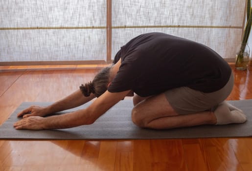 Young man in sports suit doing yoga with window with curtain in the background. Concept of yoga and meditation. Space for text.Concept of breathing, meditation and well-being.