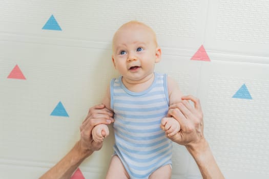 A baby lies on a soft children play mat while their father hands gently support and protect them. Heartwarming moment of care and connection. Parenthood, safety, and love concept.
