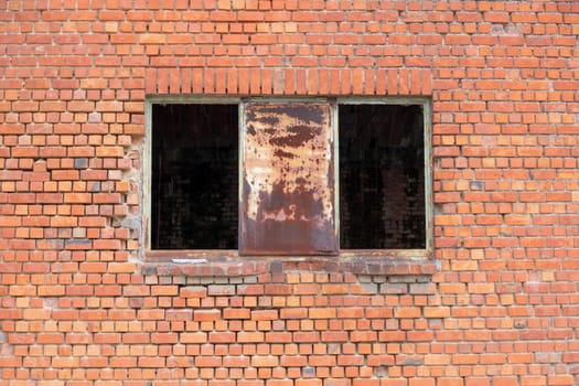 Rusty metal sheet between gaping holes in window opening in old brick wall of abandoned building, industrial decay concept, vintage architectural texture,