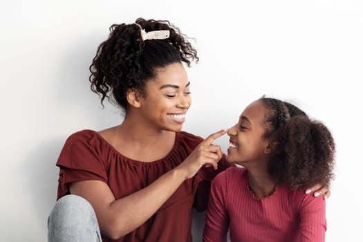 Loving african american mother spending time with her cute daughter, young black woman and teen girl sitting on floor next to empty white wall together, bonding, laughing, copy space