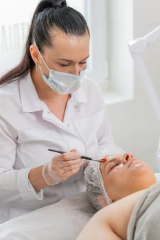 Face peeling mask, spa beauty treatment, skincare. Beautician applying vitamins moisturizing cream on young woman face for rehydrate face skin, anti aging cosmetic procedure in beauty salon. Vertical.