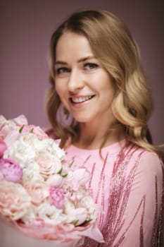 blonde hair poses with flower e, wearing a pink dress. Pink background.