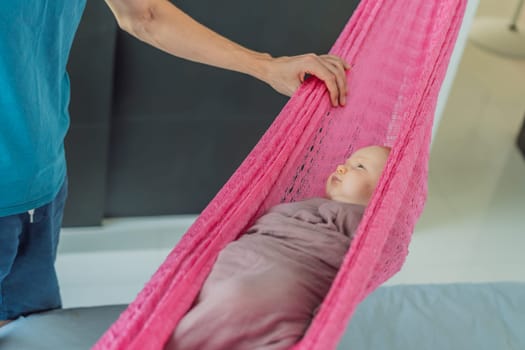 A 3-month-old baby peacefully falls asleep in a soft muslin swaddle while cradled in a cozy hammock. A serene and tender moment of comfort and relaxation. Baby care, rest, and tranquility concept.