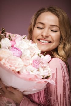 blonde hair poses with flower e, wearing a pink dress. Pink background.
