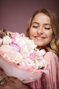 blonde hair poses with flower e, wearing a pink dress. Pink background.