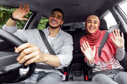 Happy smiling millennial islamic lady in hijab and man singing, dancing and enjoying travel in car cabin together, outdoor, free space. Good mood, buying new car, weekend trip and road at journey